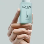 Hand model holding L’Oreal beauty serum on a pastel blue background