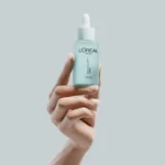 Hand model holding L’Oreal serum against a pastel blue background