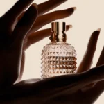 Hand modeling with Valentino textured perfume bottle on beige background