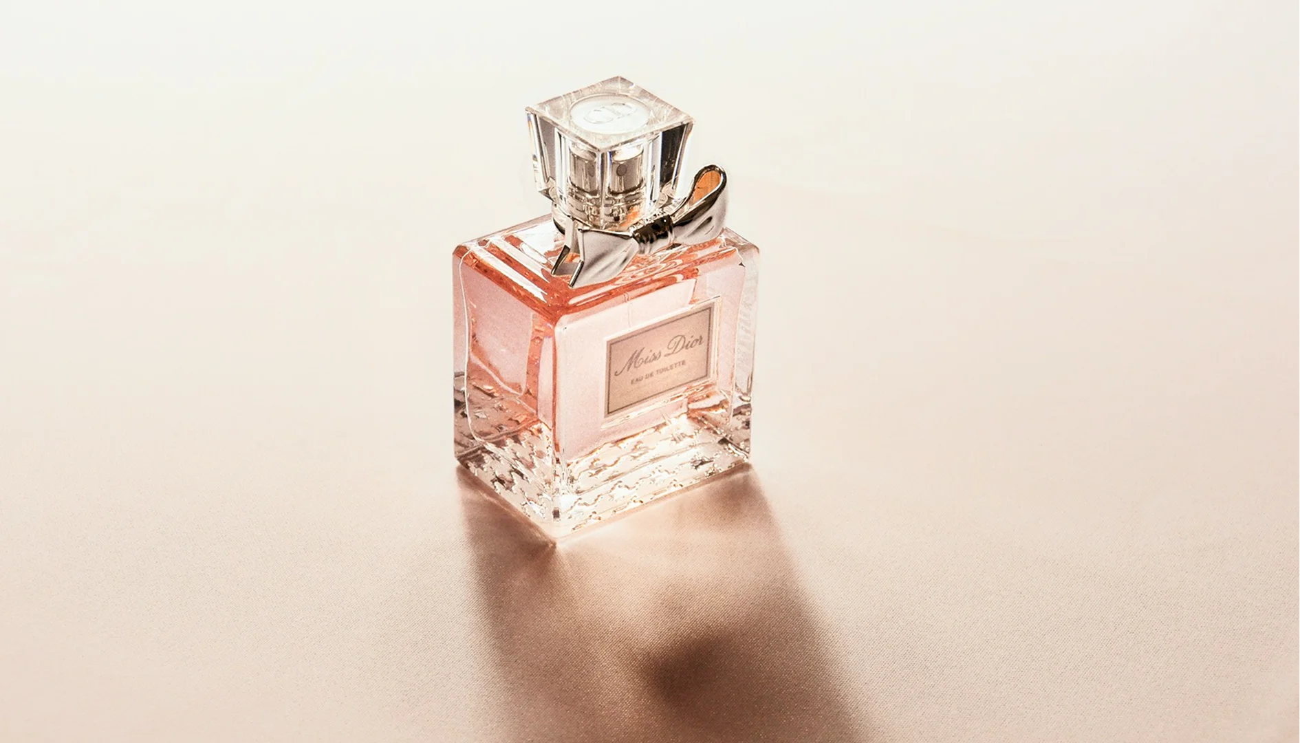 Miss Dior perfume bottle photographed on a textured, champagne-colored satin fabric background