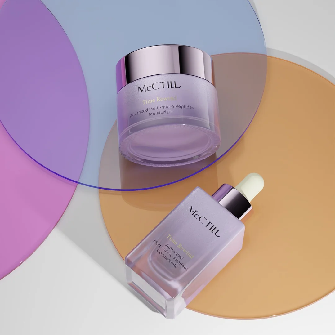 A top-down shot of a skincare jar and bottle resting on overlapping translucent acrylic disks in shades of purple, blue, and amber orange