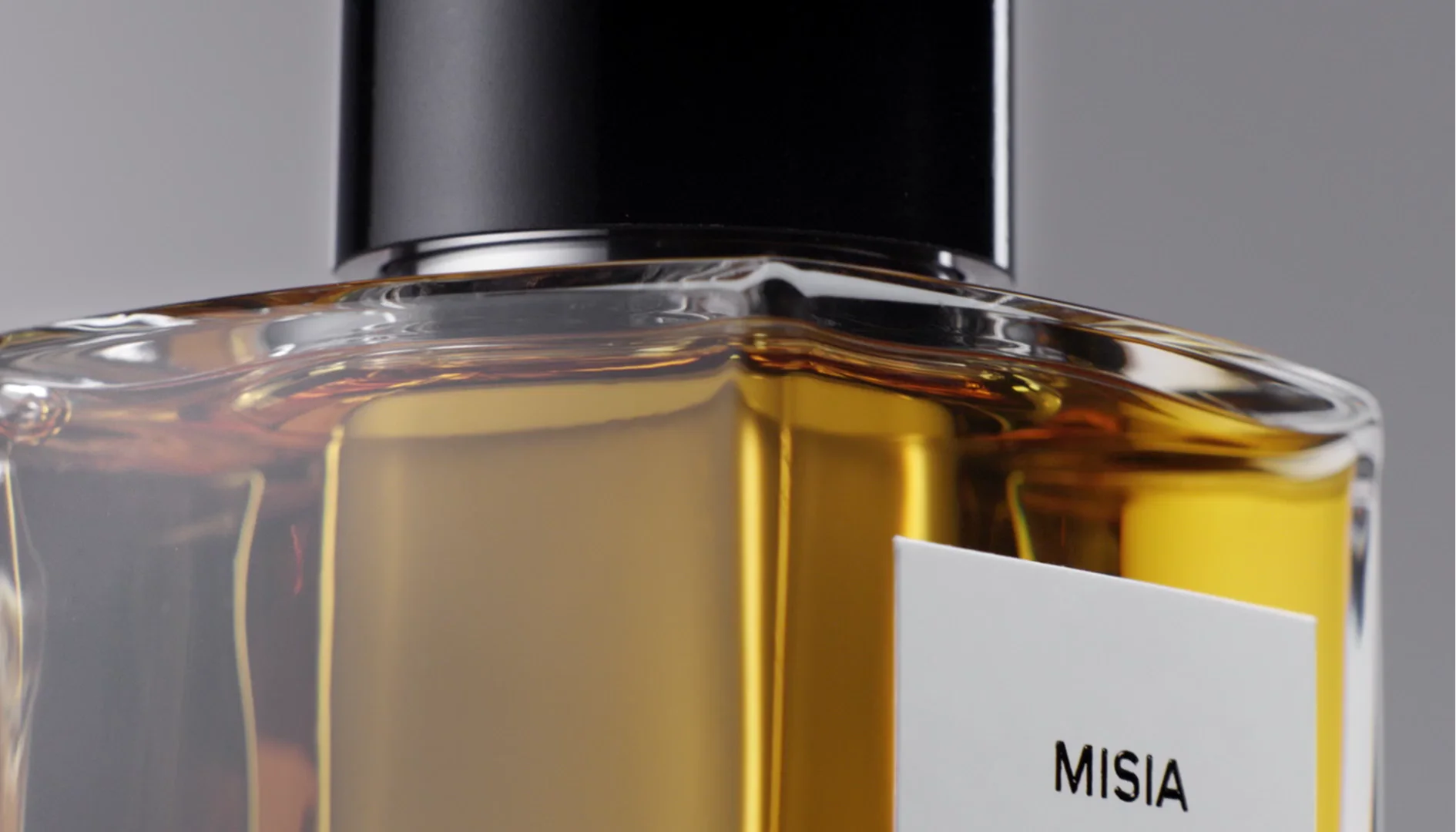 Close-up macro shot of a perfume bottle highlighting light refraction through thick glass and golden liquid.